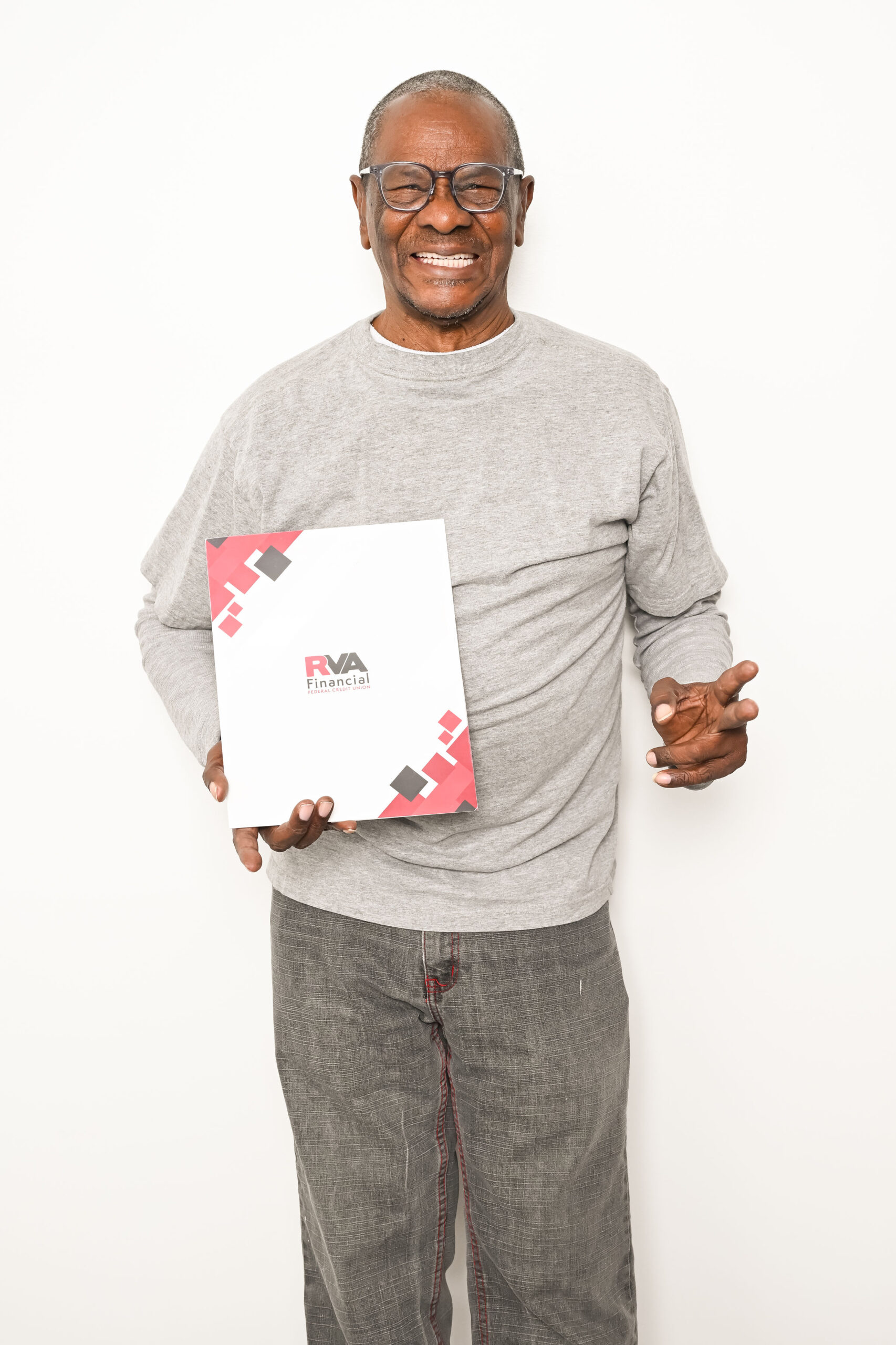 Smiling man wearing glasses and a gray long-sleeve shirt holds a folder labeled RVA Financial against a plain white background.